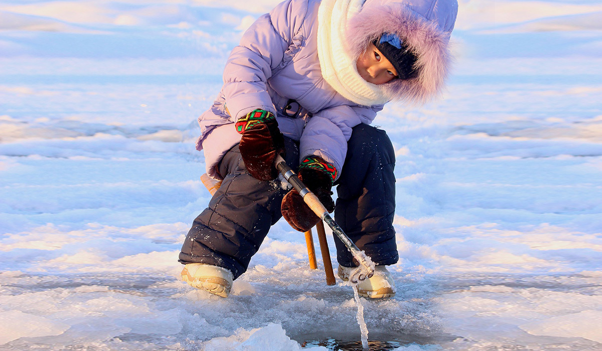 En flicka som sitter på isen och fiskar